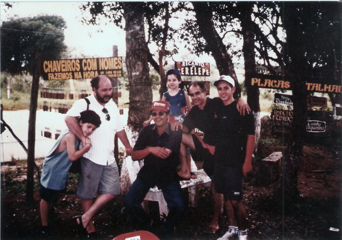 Edélcio com a família e amigos na feirinha da rodovia Bunjiro Nakao em Ibiúna, verão de 1998. Ao fundo, placas 'Chaveiros com Nomes' e 'Placas Entalhadas'